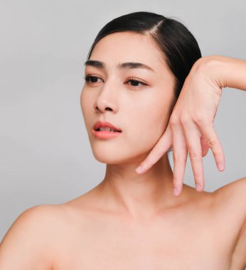 Temiz ve parlak ciltli genç Asyalı kadın, Kozmetik Güzellik Konsepti, yanağına dokunan eller, gri arka planda izole edilmiş gülen ve arkadaş canlısı yüz.