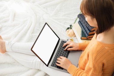 Güzel Asyalı kısa saçlı kız turuncu kazak giyer, müzik dinler ve tatilde kitap okurdu. Otur ve bir kitap oku, dizüstü bilgisayarla çalış.