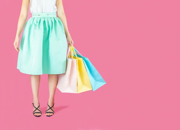 The  woman low body part wore blue skirt and black high heels. Carrying a shopping bag in many pastel colors on pink background selective focus