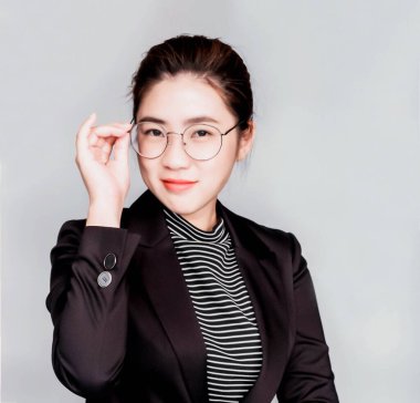 Genç zeki, güzel Asyalı iş kadını siyah takım elbise ve gözlük takmış, akıllı ve düşünceli. Belge tutuyor, telefonla konuşuyor.