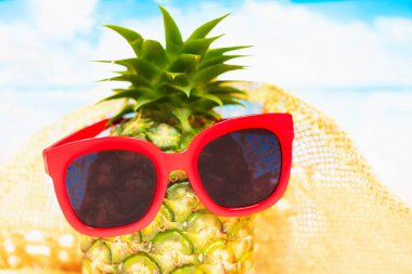 Plaj, kırmızı güneş gözlüklü komik ananas ve deniz ve gökyüzüne karşı kumun üzerinde şapka. Tropik yaz tatili konsepti. Kumsalda güneşli bir gün seçici odak noktası sarı ve mavi deniz.