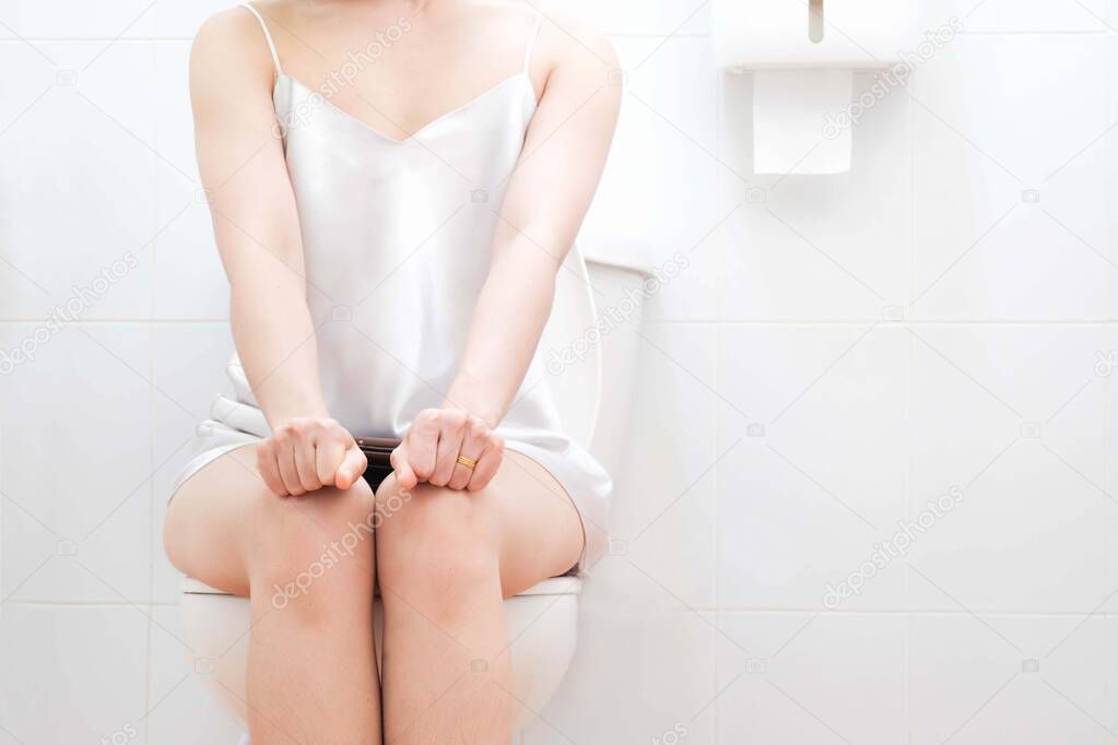 Women wearing white sleepwear, Sitting on the toilet Hand holding the stomach,standing in the toilet, Holding a toilet paper, bent, stomachache health care concept
