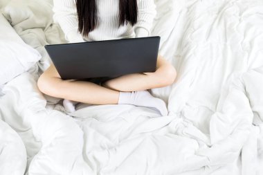Seçici odaklanma. Genç Asyalı bir kadının vücudu yatağa beyaz örgü elbise giyer, online yaşam tarzı çalışır. Evde dinlenir, beyaz battaniye fotokopisi çekilir.
