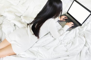 Seçici odaklanma. Genç Asyalı bir kadının vücudu yatağa beyaz örgü elbise giyer, online yaşam tarzı çalışır. Evde dinlenir, beyaz battaniye fotokopisi çekilir.