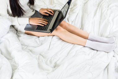 Seçici odaklanma. Genç Asyalı bir kadının vücudu yatağa beyaz örgü elbise giyer, online yaşam tarzı çalışır. Evde dinlenir, beyaz battaniye fotokopisi çekilir.