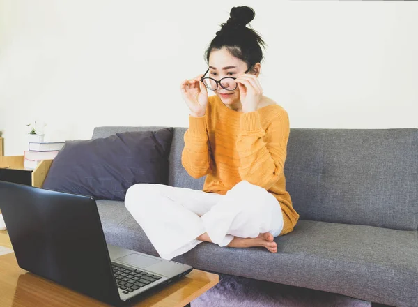 soft selective focus young beautiful asian woman wore orange knitwear,sitting on gray sofa,work online lifestyle,relax at home with coffee,home working laptop,work from home