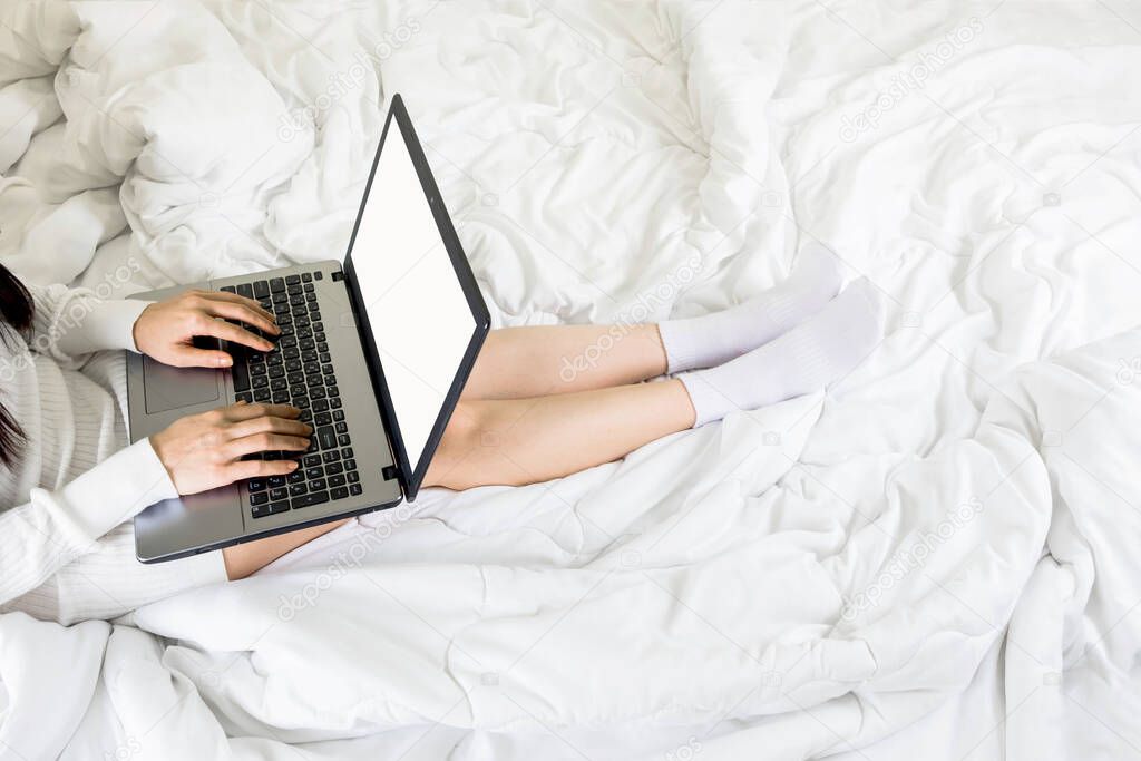 Selective focus a body part of young asian woman wear white knitwear dress and socks on bed,work online lifestyle with blank screen laptop relax at home ,white blanket copy space