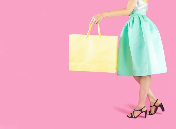 woman low body part wore blue skirt and black high heels. Carrying a shopping bag in many pastel colors on pink background selective focus