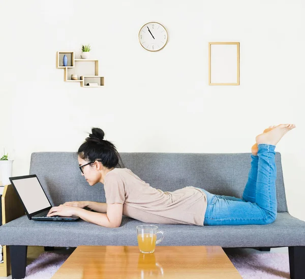 Young beautiful asian woman wore brown t shirt and jean, lying and sitting on gray sofa ,work online lifestyle,relax at home with coffee mug,home working laptop,work from home