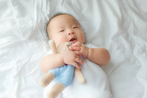 top view Portrait of a newborn Asian cute baby boy wore blue Infant bodysuit on the bed , Charming Fat baby 5 month old lies in bed with a doll,enjoy and happy