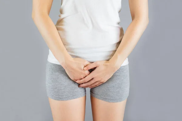 woman wore gray shorts put her hand on the genitalia area.female with hands holding her Penis in pain.Health-care Concept.Selective focus isolated on gray background