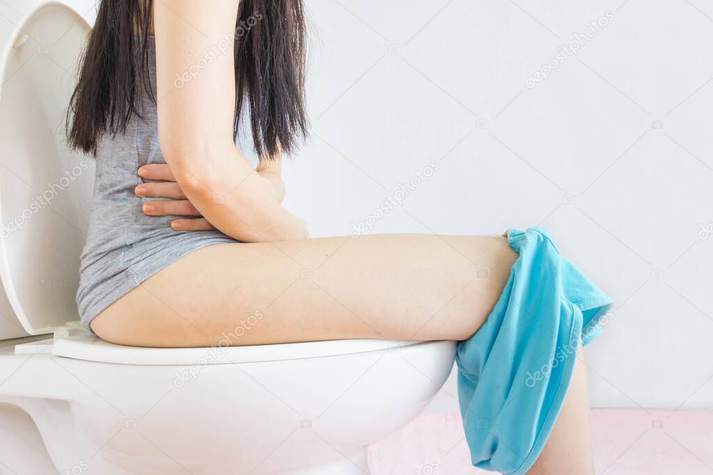 young asian woman wore gray undershirt and blue shorts was sitting in the toilet,hand holding the stomach,health care concept
