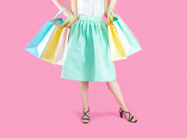The woman low body part wore blue skirt and black high heels. Carrying a shopping bag in many pastel colors on pink background selective focus