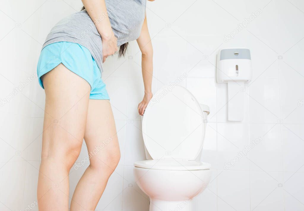 Young asian woman wore gray undershirt and blue shorts was standing in the toilet,The body is bent, the hand is held in the stomach.health care concept