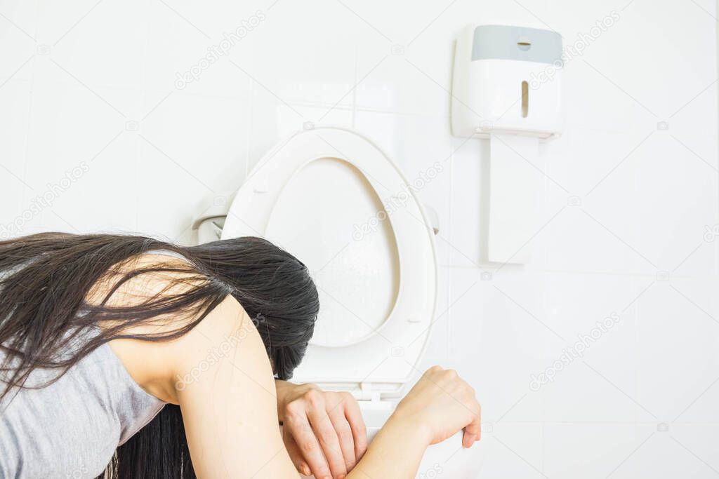 Young woman vomiting into the toilet bowl in the early stages of pregnancy or after a night of partying and drinking