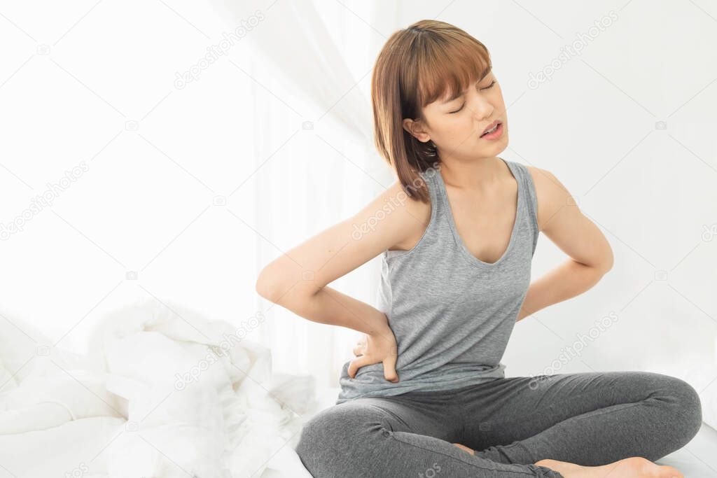 young beautiful asian woman wearing gray clothes,Wake up in a white bed in the morning, The body aches, Hug hands on the stomach Curled up with abdominal pain, stomachache,pain,painful