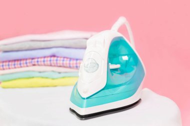 Modern Elektrik Ütüsü ve çamaşır odasındaki pembe arka planda ütü masasında bir yığın kıyafet. Çamaşırları ütüleyen kadın katlanmış ve kurumuş çamaşır yığınları tutuyor.