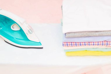 Modern Elektrik Ütüsü ve çamaşır odasındaki pembe arka planda ütü masasında bir yığın kıyafet. Çamaşırları ütüleyen kadın katlanmış ve kurumuş çamaşır yığınları tutuyor.