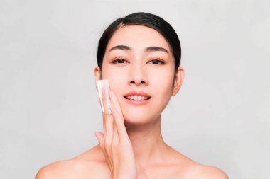 Temiz ve parlak ciltli genç Asyalı kadın, Kozmetik Güzellik Konsepti, yanağına dokunan eller, gri arka planda izole edilmiş gülen ve arkadaş canlısı yüz.
