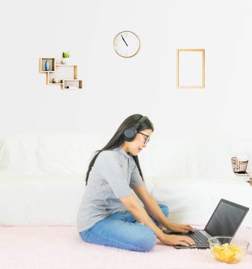 yumuşak seçici odak Genç güzel Asyalı kadın gri t-shirt giydi ve kot pantolon, oturma odasında pembe halı üzerinde oturuyor, online yaşam tarzında çalışıyor, kahve fincanıyla evde dinleniyor, ev bilgisayarı ile çalışıyor, evden çalışıyor.