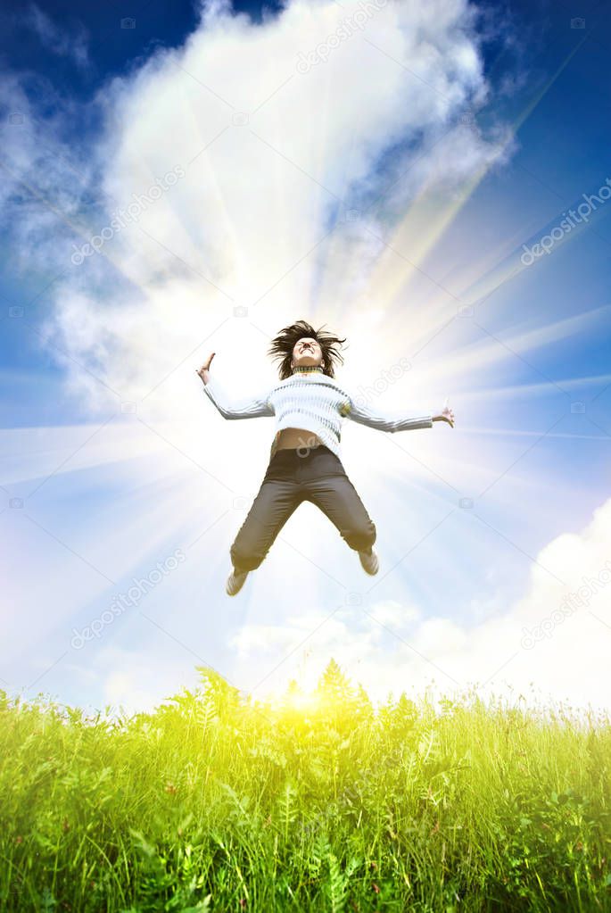 Young woman jumping into the field against the blue sky