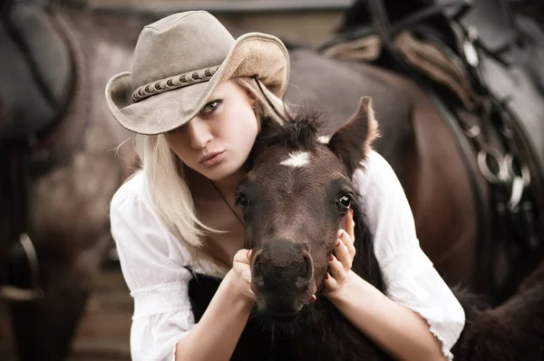 Sexy lächelnde Frau mit Cowboyhut umarmt ein Fohlen — Stockfoto