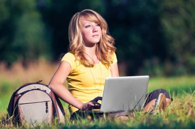 Yeşil çimenlerin üzerinde dizüstü bilgisayar ile oturup güzel kız
