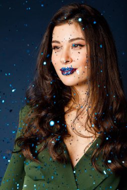 Mavi arka planda dudaklarında mavi konfeti olan esmer bir kızın portresi.