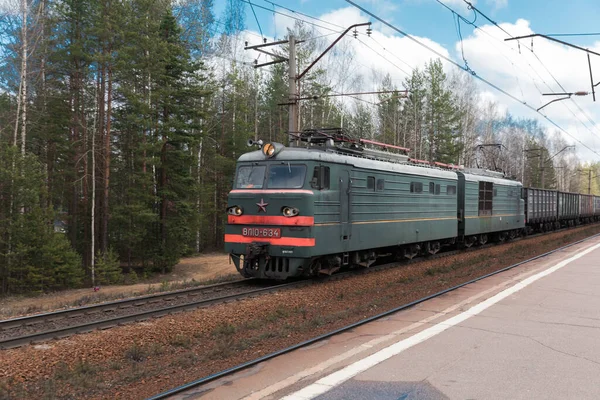 Ormanın arka planında elektrikli bir lokomotif tarafından çekilen yük treni.