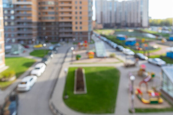 Blurred courtyard of a large multi-storey residential complex in summer with parking spaces for cars. Blurred basic bokeh background for design.