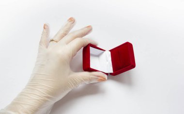 Karantinaya alınmış düğün. Coronavirus nikahı. Beyaz arka planda alyansı olan tıbbi bir eldivenin içinde evlilik yüzüğünün yanındaki kırmızı kadife kutunun içinde.