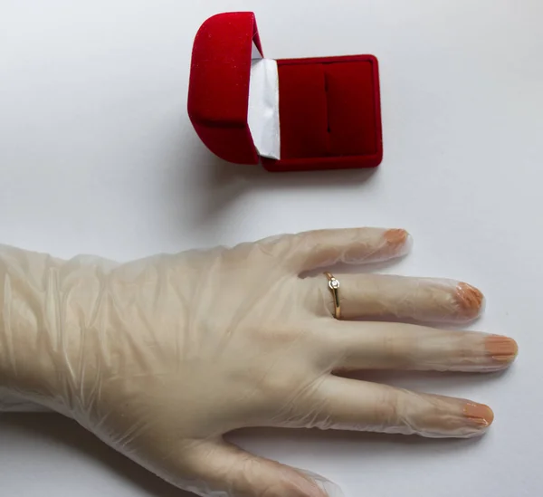 Karantinaya alınmış düğün. Coronavirus nikahı. Beyaz arka planda alyansı olan tıbbi bir eldivenin içinde evlilik yüzüğünün yanındaki kırmızı kadife kutunun içinde.