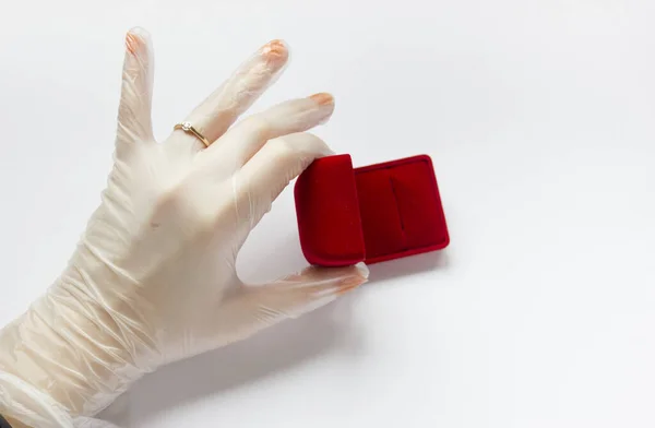 Karantinaya alınmış düğün. Coronavirus nikahı. Beyaz arka planda alyansı olan tıbbi bir eldivenin içinde evlilik yüzüğünün yanındaki kırmızı kadife kutunun içinde.