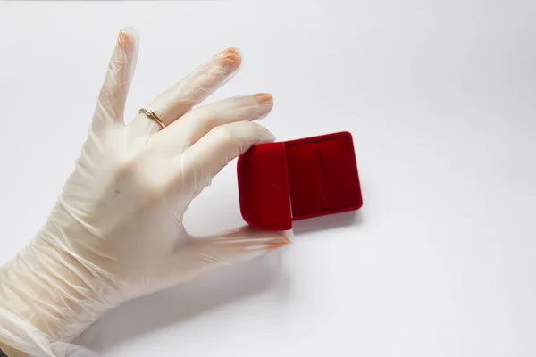 Karantinaya alınmış düğün. Coronavirus nikahı. Beyaz arka planda alyansı olan tıbbi bir eldivenin içinde evlilik yüzüğünün yanındaki kırmızı kadife kutunun içinde.