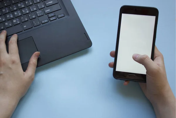 man works at a laptop and holds a phone in his hand flatly.the problem of concentration at work while working from home.man distracted by phone while working from home on laptop.