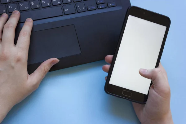 man works at a laptop and holds a phone in his hand flatly.the problem of concentration at work while working from home.man distracted by phone while working from home on laptop.