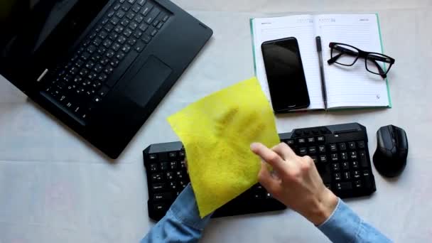 Una persona sentada en un escritorio con un ratón y un teclado de computadora. un hombre rocía un antiséptico en una servilleta y limpia el teléfono — Vídeo de stock