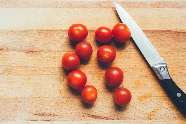 Vibrant cherry tomato and kitchen knife on a wooden chopping board lying on gray linen tablecloth. Stylish graceful picture. Photos for food recipes.Knife and cherry tomatoes lie on a wooden board.