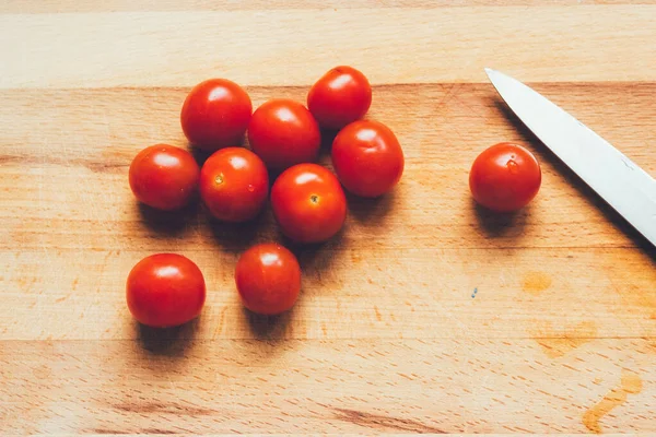 Knife and cherry tomatoes lie on a wooden board.Vibrant cherry tomato and kitchen knife on a wooden chopping board lying on gray linen tablecloth. Stylish graceful picture. Photos for food recipes.