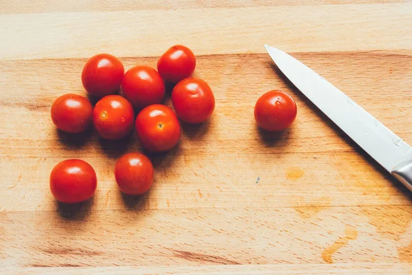 Knife and cherry tomatoes lie on a wooden board.Vibrant cherry tomato and kitchen knife on a wooden chopping board lying on gray linen tablecloth. Stylish graceful picture. Photos for food recipes.