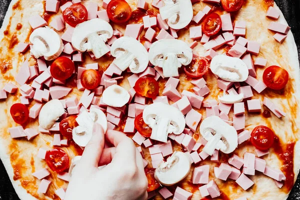 Ev yapımı pizza. Adım adım. Pizzanın 6.basamağı. Genç kızın eli, domates, sosis ve mantarlı çiğ pizzanın üzerine domates dilimi koyuyor..