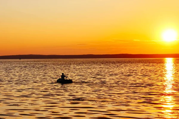 Şişme bir teknede erkek bir balıkçı silueti gün batımında Volga 'da yüzer. Kıyıdan Volga nehri manzarası. Volga Nehri Günü 20 Mayıs. Rusya.