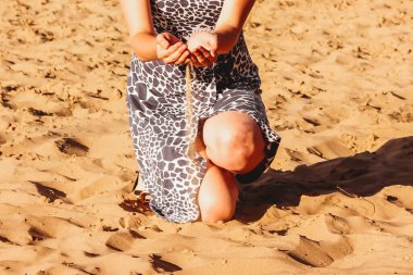 Kadın elleri kumsala kum döküyor. Çok sığ bir alan derinliği ve hareket bulanıklığı. Palmiyelerden kum döken bir kız..