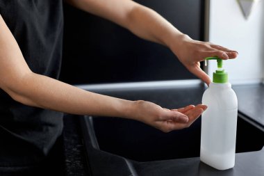 Kadın, ellerini yıkamak için siyah mutfak arka planında sabun kullanıyor.