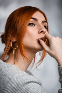 Yakın plan kızıl saçlı, gri kazaklı, omuzları açık genç bir kadın. Düşünceli bir şekilde uzaklaşıyor.