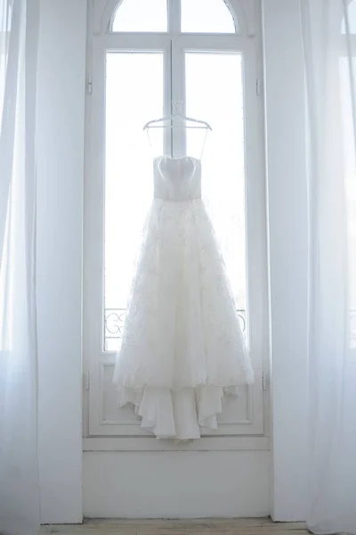 Перфектное свадебное платье с полной юбкой и поездом, бессонное на вешалке в комнате для невест с белыми шторами . — стоковое фото