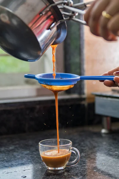Plastik süzgeçten geçip cam fincana buharlı masala çayı döken bir el.