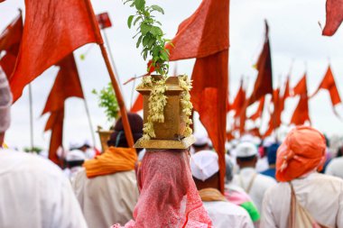 pilgrimage - a woman carrying a holy basil plant pot over her head with others carrying an orange flag clipart