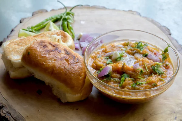 Gri arka planda ahşap bir tabakla süslenmiş ve çiğ soğan limonuyla süslenmiş Hint sokak yemekleri pav bhaji.