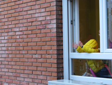 Coronavirus karantinası sırasında bir çocuk pencerede el çırpıyor.
